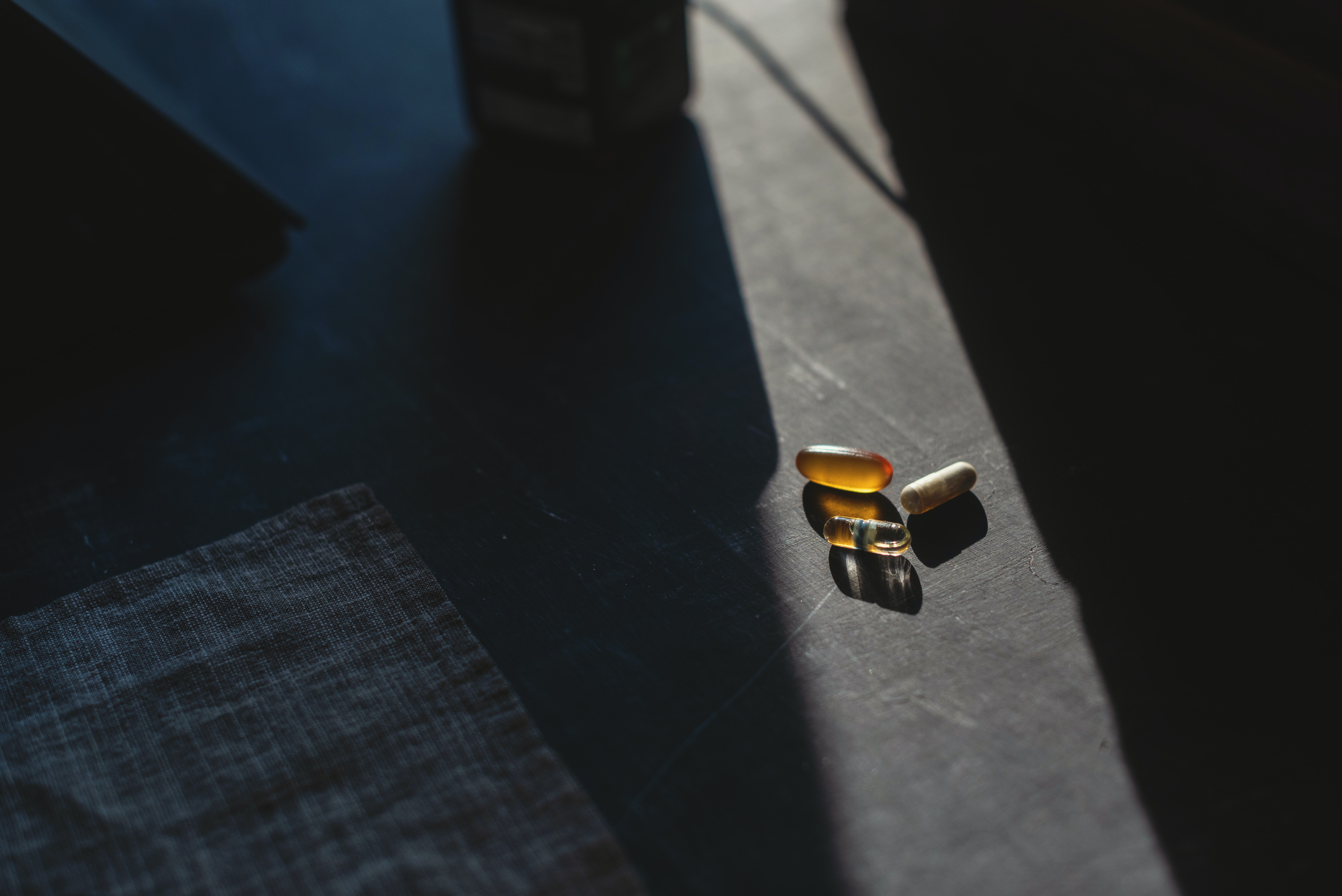 Three pills on dark grey background highlighted by natural light